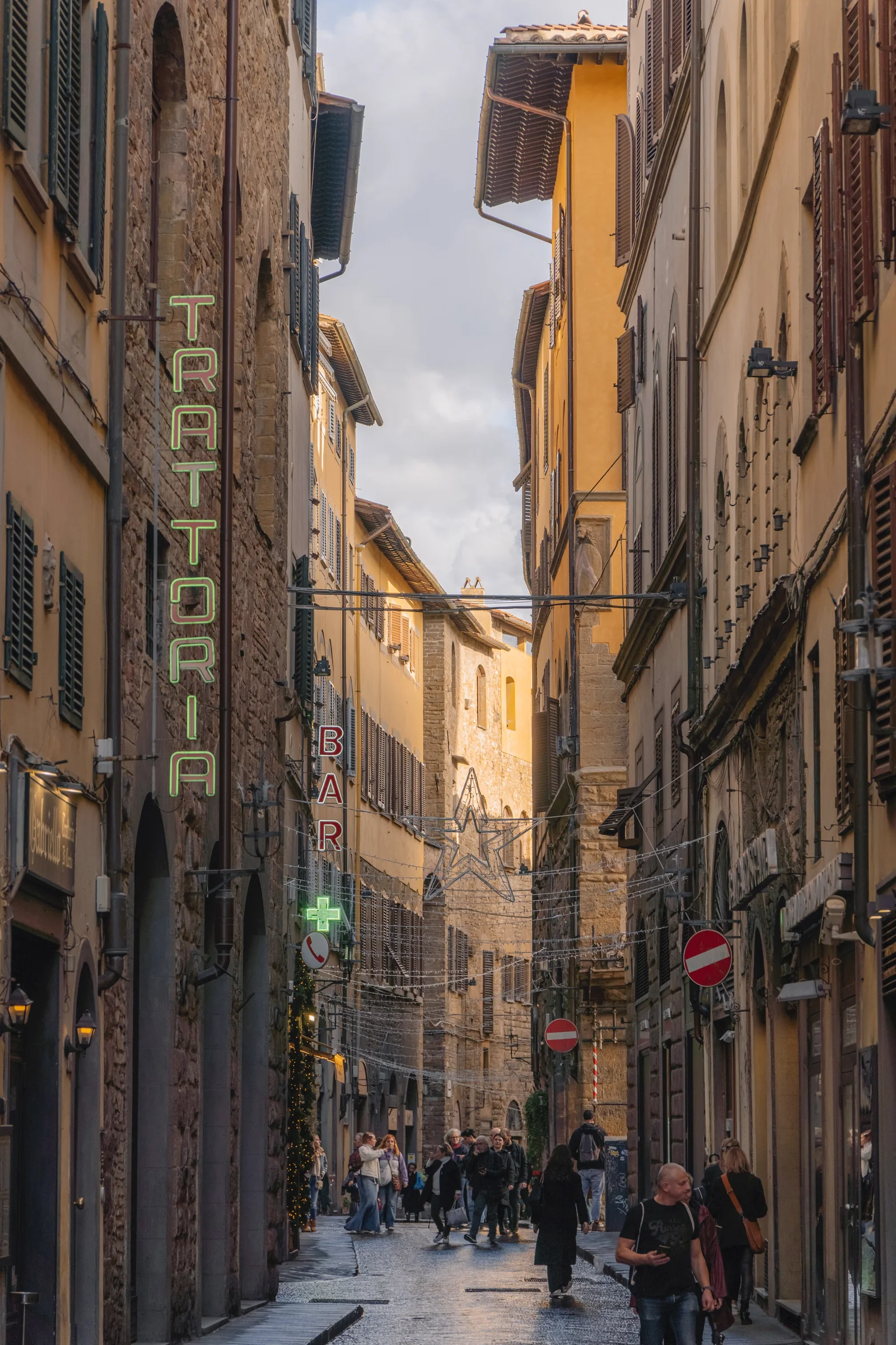 Narrow Florentine lane with neon Trattoria and Bar signs and a hanging star light