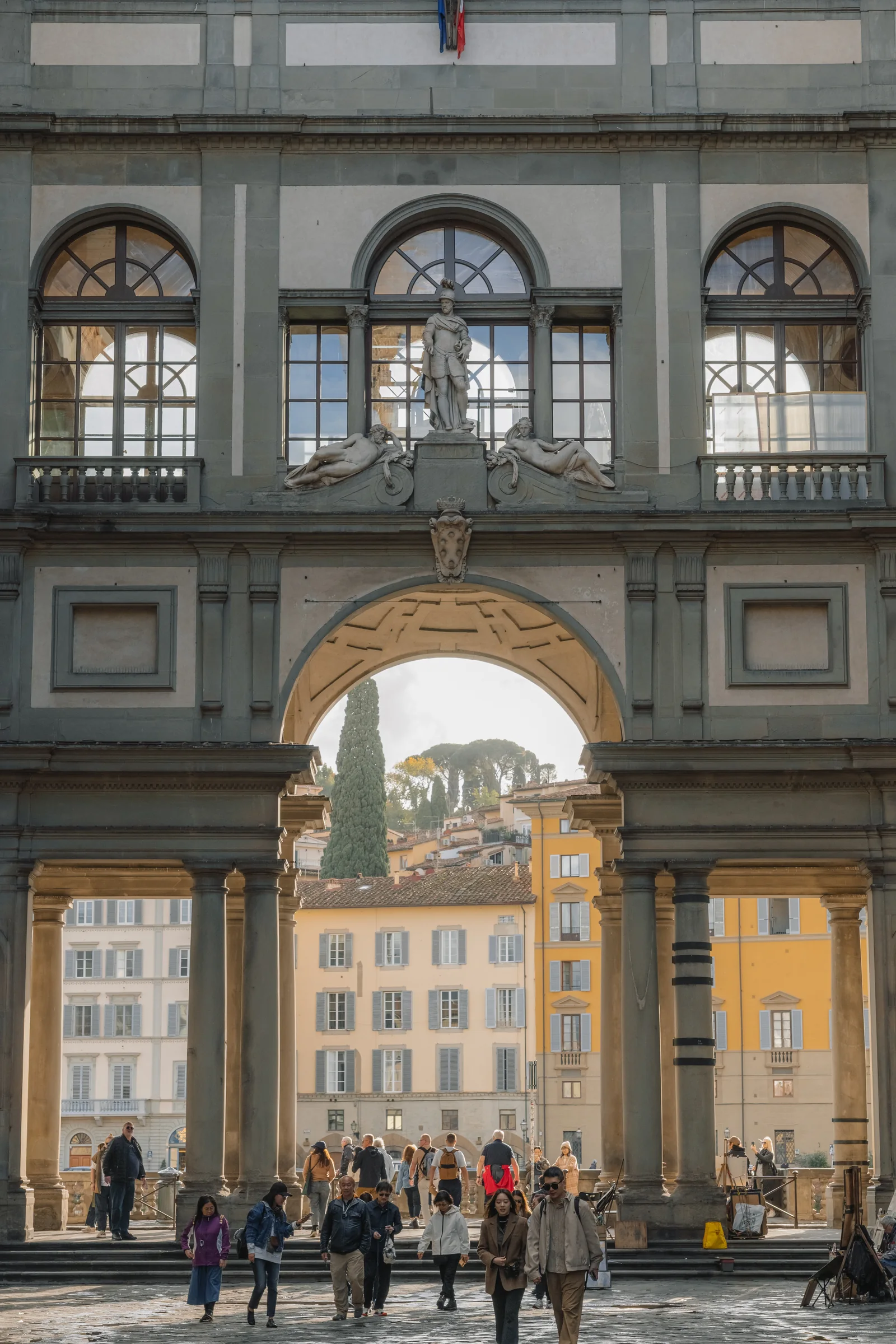 Arched opening of the Uffizi loggia framing cypress and rooftops beyond