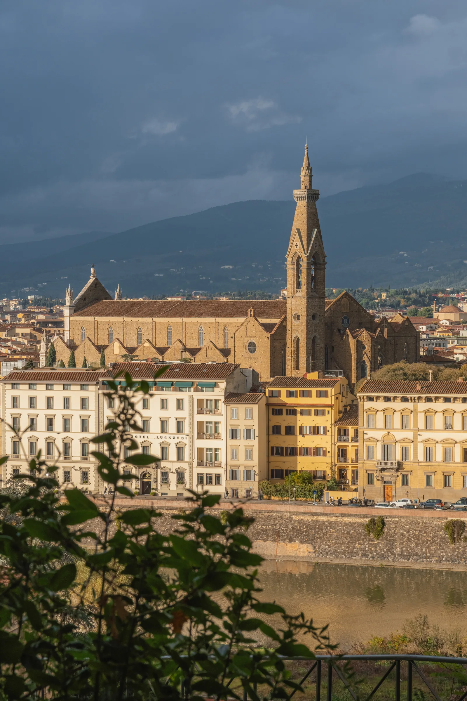 Basilica of Santa Croce catching low sun against dark storm clouds and hills