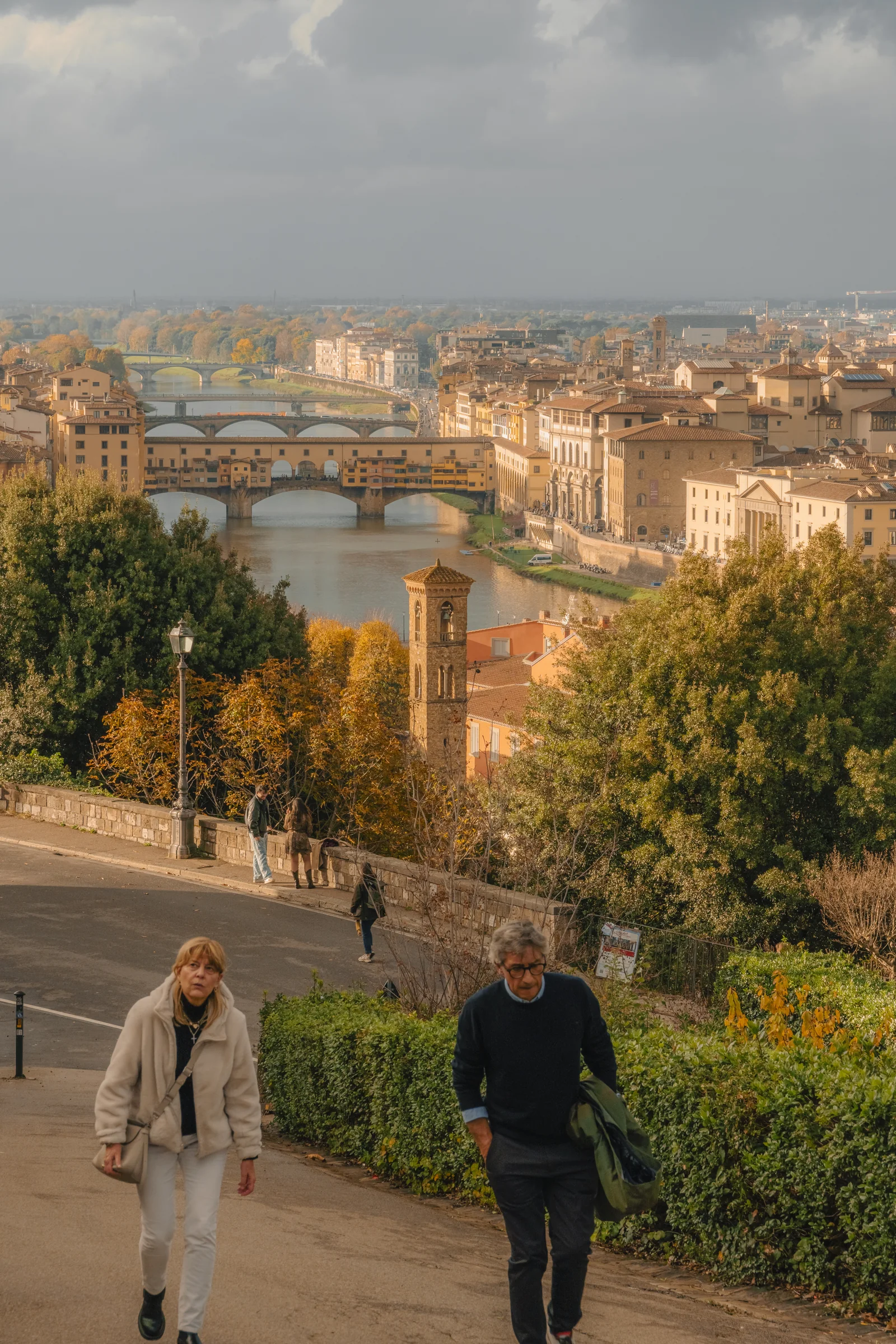 Couple climbing a path above the Arno with Ponte Vecchio and the bridges beyond