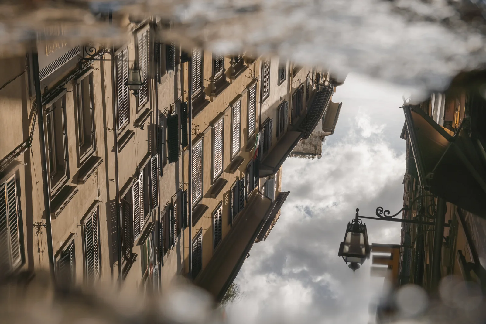 Shuttered facades and a wrought-iron lantern mirrored in a street puddle
