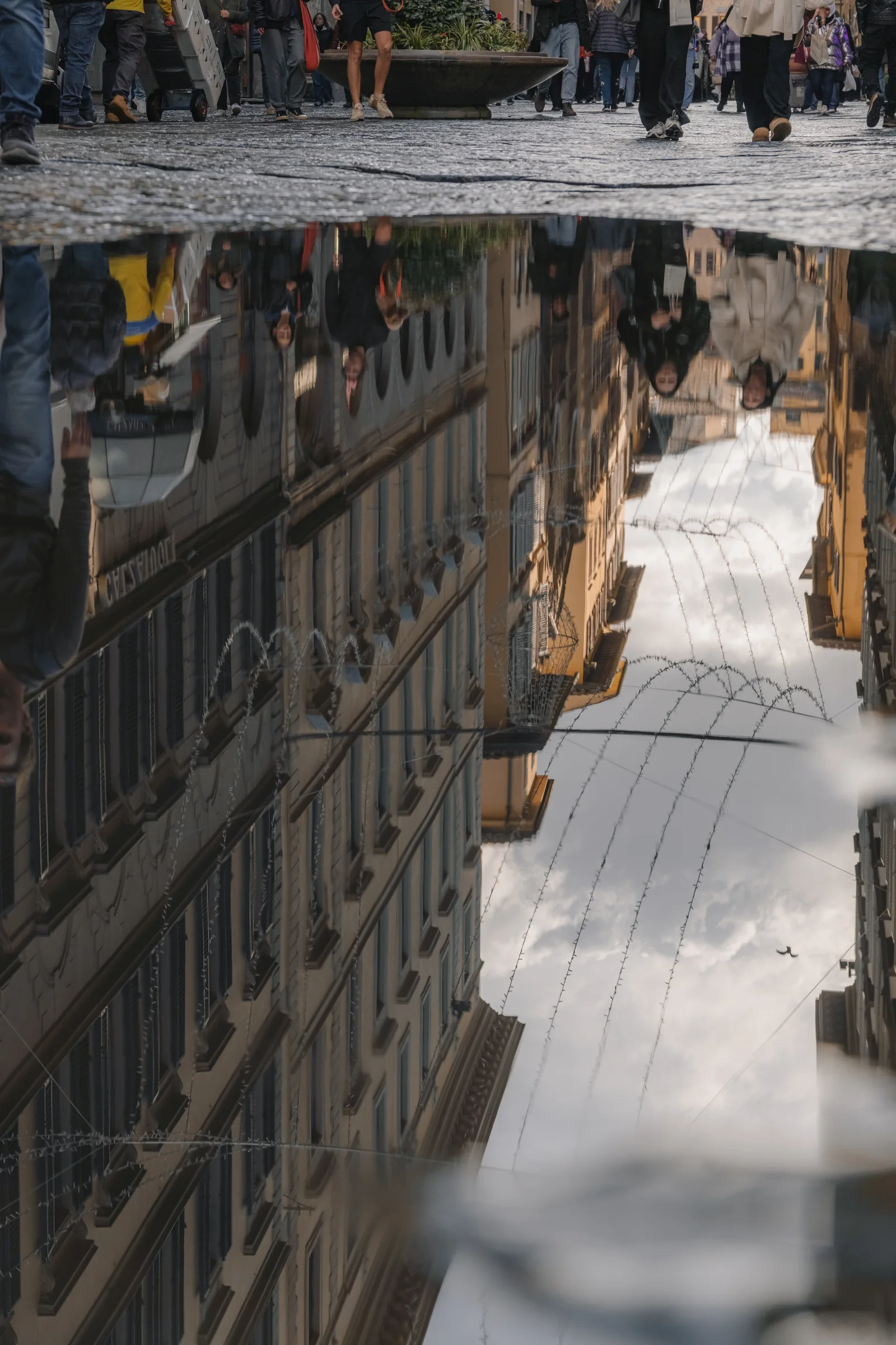 Upside-down puddle reflection of a crowded street strung with fairy lights