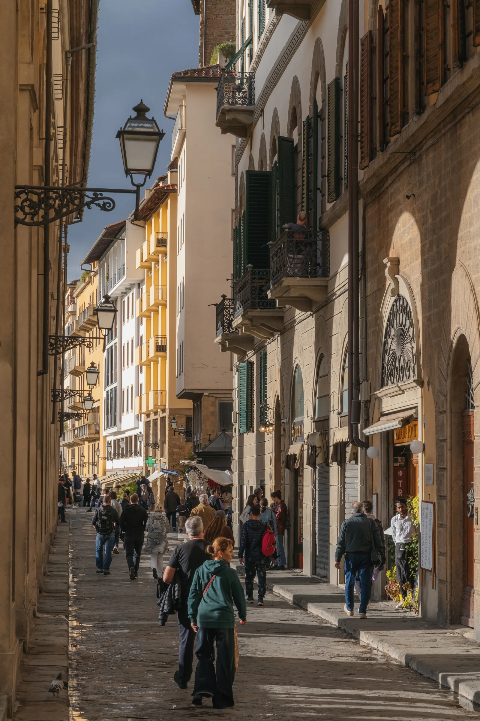 Busy lane near Ponte Vecchio lined with iron street lamps and balconies