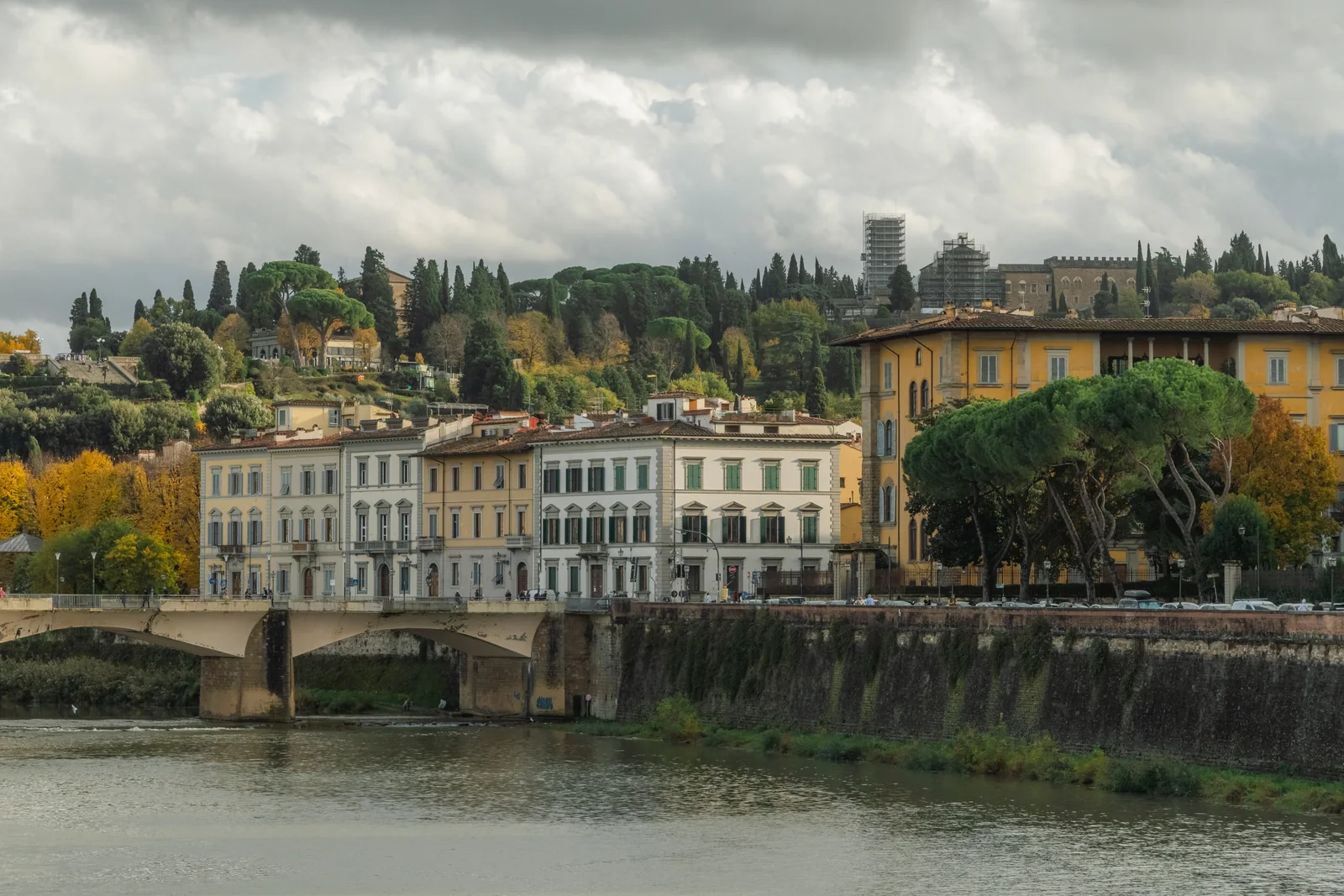 The Arno below a hillside of cypress and villas, a bridge and the long embankment wall under low cloud