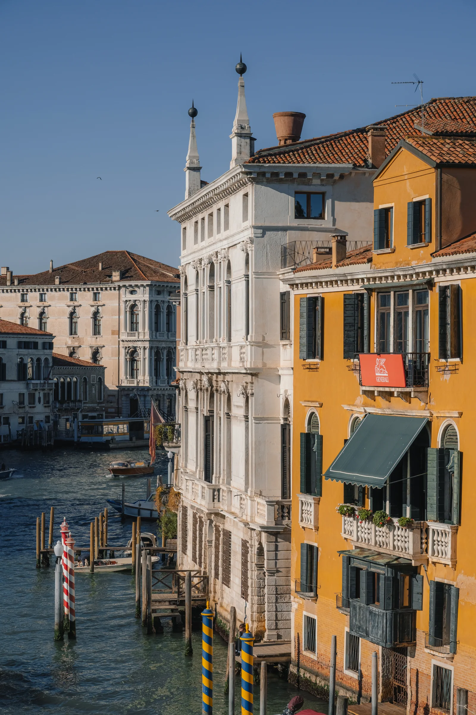 Grand Canal palazzi in morning sun, a white marble facade beside an ochre house with striped mooring poles