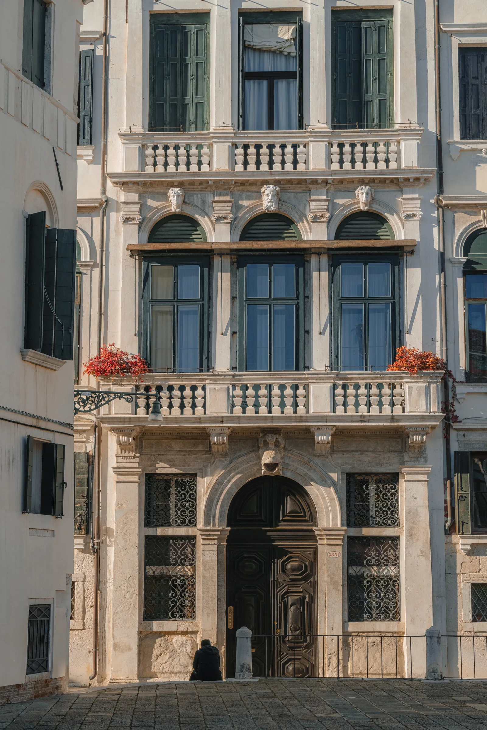 An ornate Venetian palazzo facade with mascarons and a grand doorway, a lone figure resting below