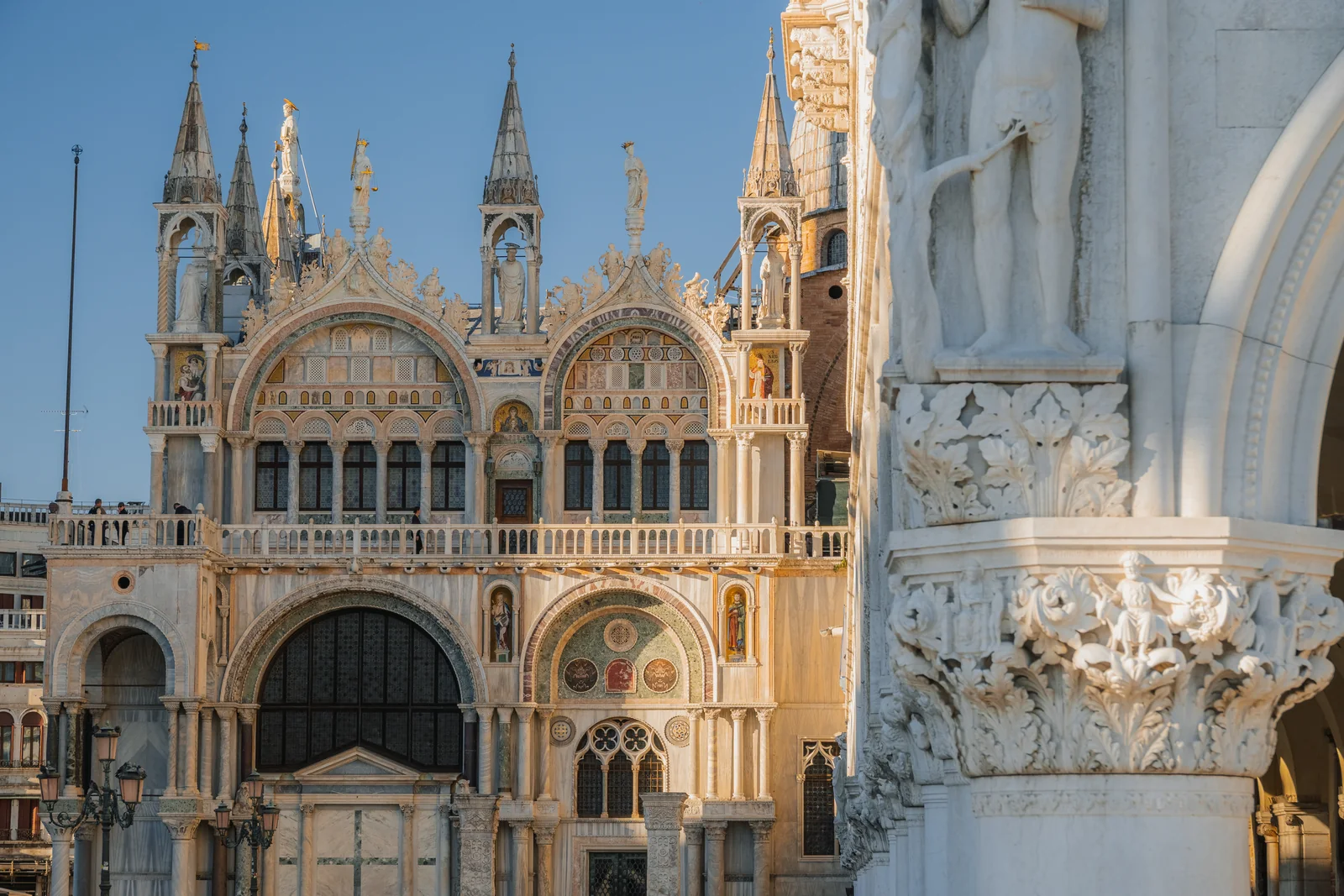 Morning light on the mosaics and spires of St Mark's Basilica beside a carved column of the Doge's Palace