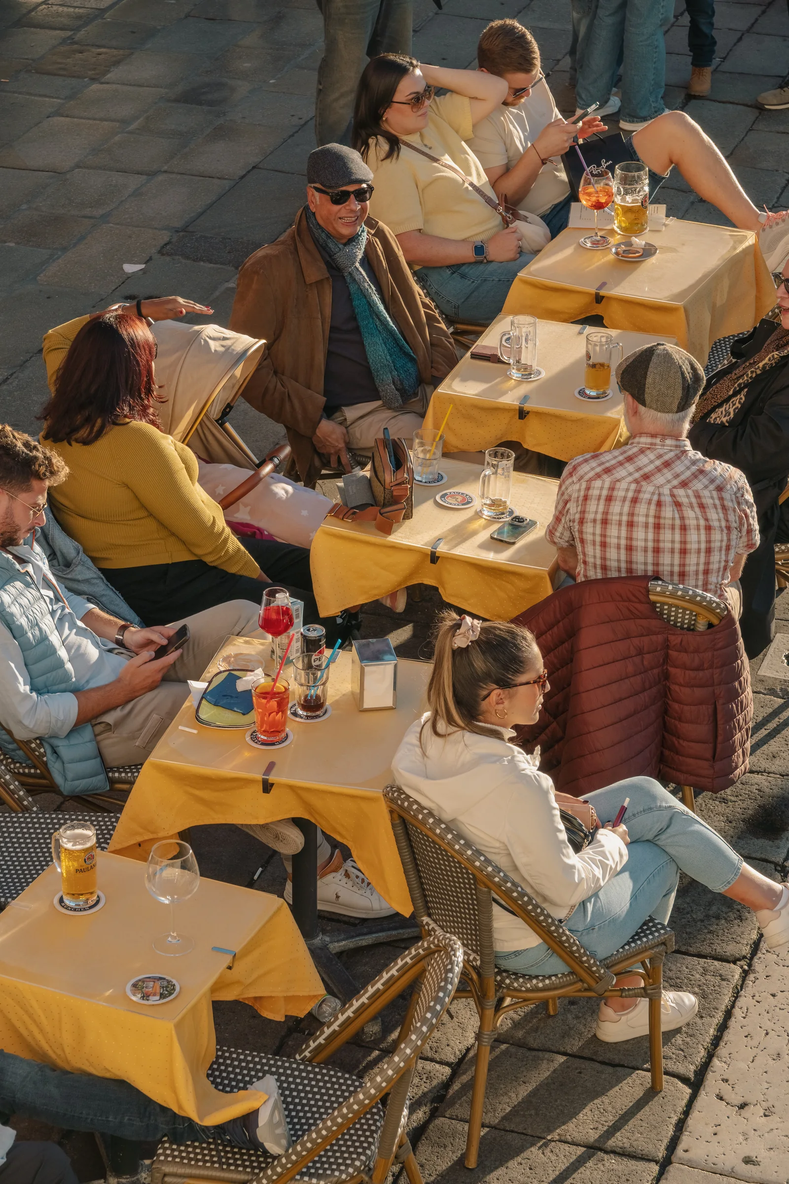 Diners at yellow-clothed cafe tables in the afternoon sun, spritz and beer on the table