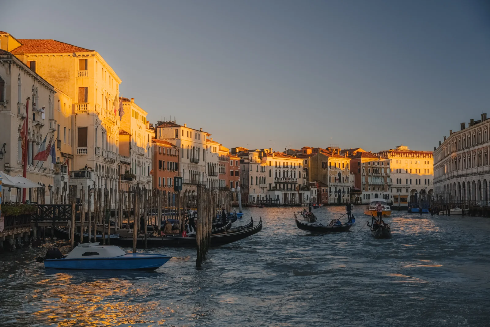 The Grand Canal at dusk, gondolas and a blue boat on the water as the facades catch the last gold