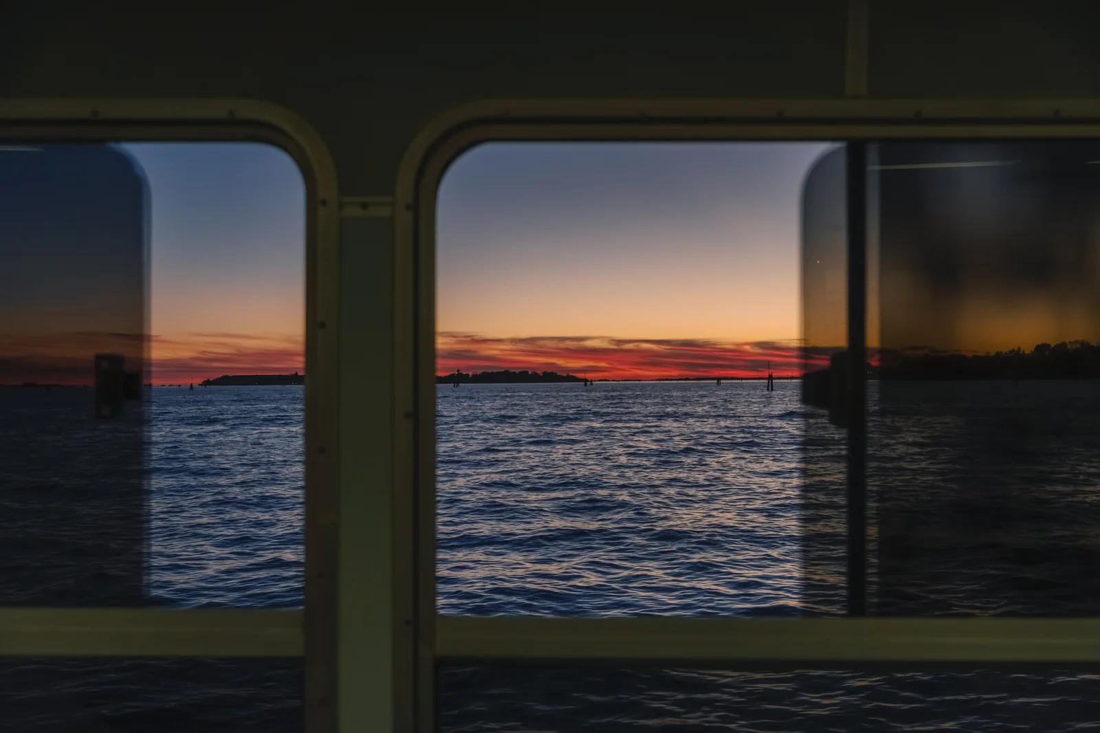 A red-and-blue lagoon sunset framed through the window of a vaporetto