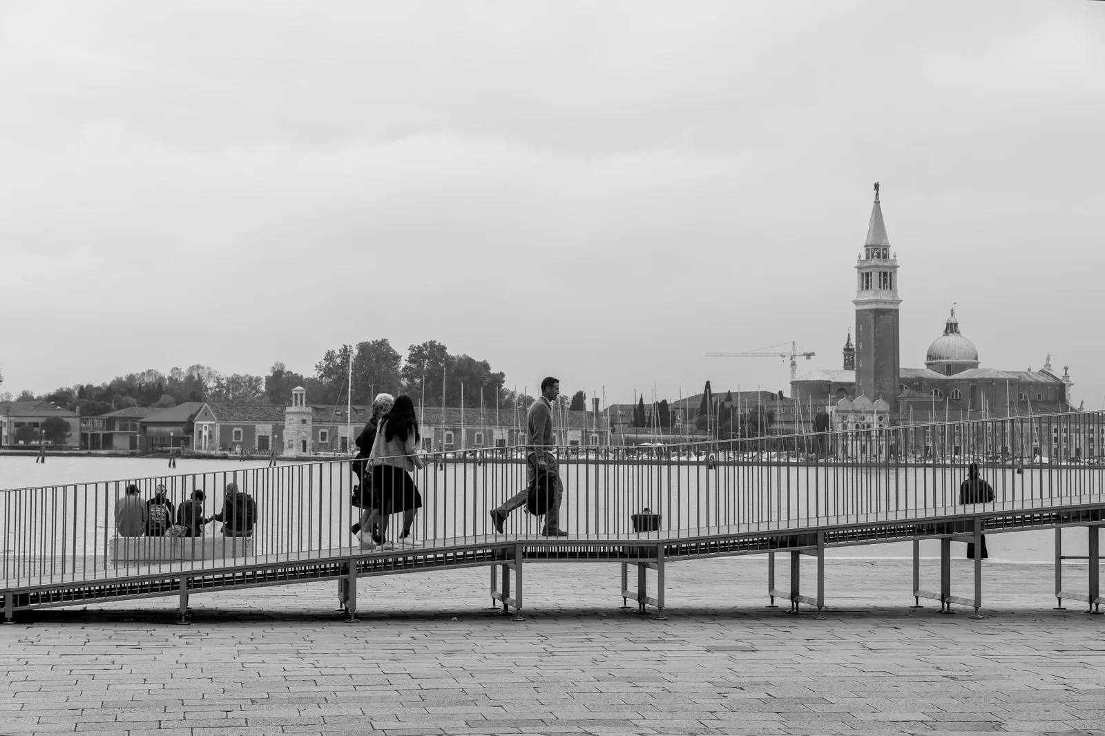 Black-and-white: people crossing a ramp on the waterfront with San Giorgio Maggiore beyond