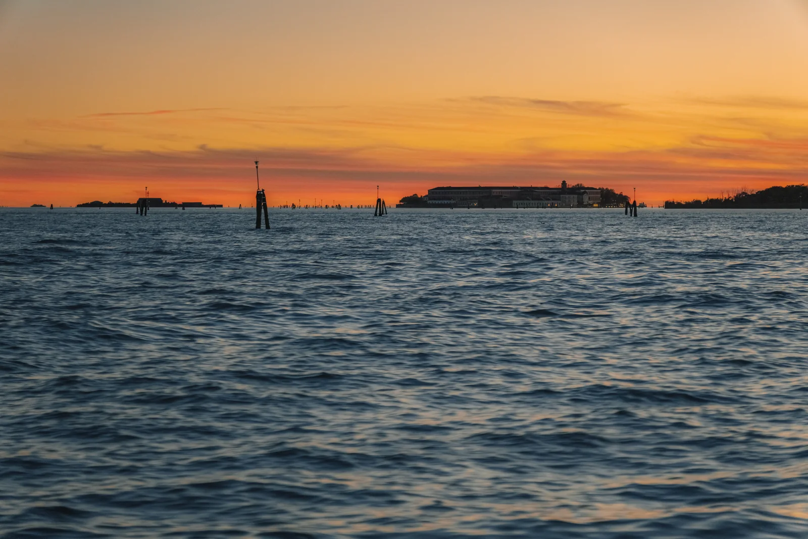 The lagoon at sunset, a low island and mooring posts under a band of orange light