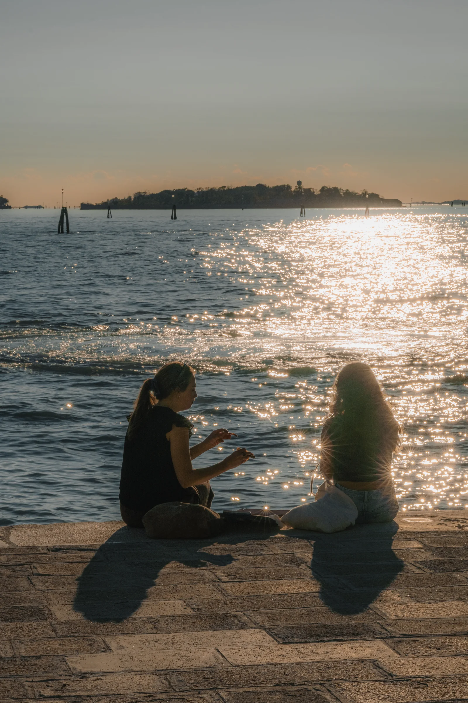 Two friends sitting on the fondamenta in the late sun, the water a sheet of sparkling light