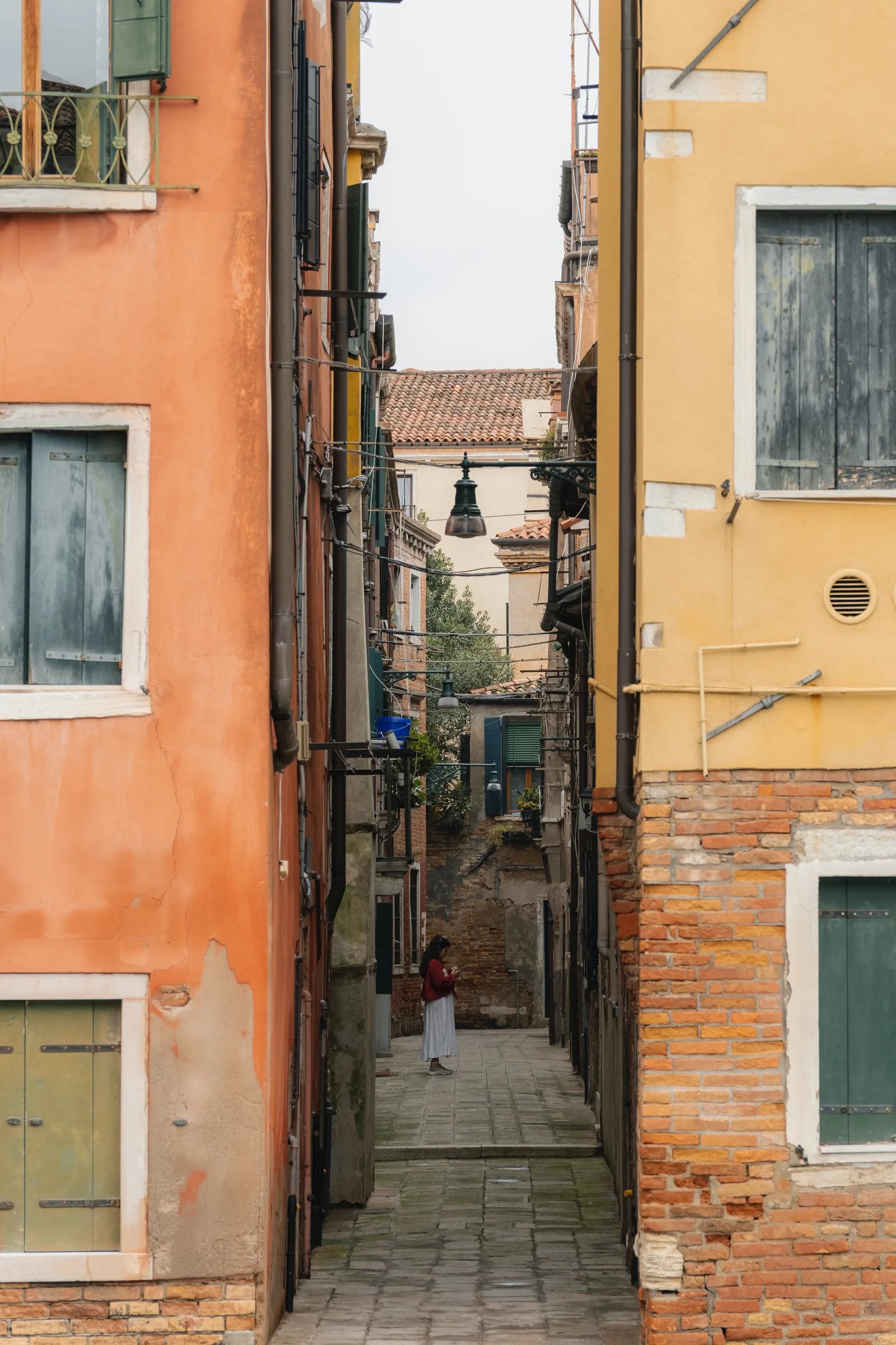 A narrow Venetian calle between ochre and brick walls, a lone figure at the far end