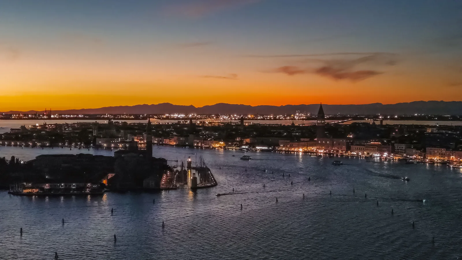 Aerial view of Venice at dusk, the lagoon and city lights coming on under an orange afterglow